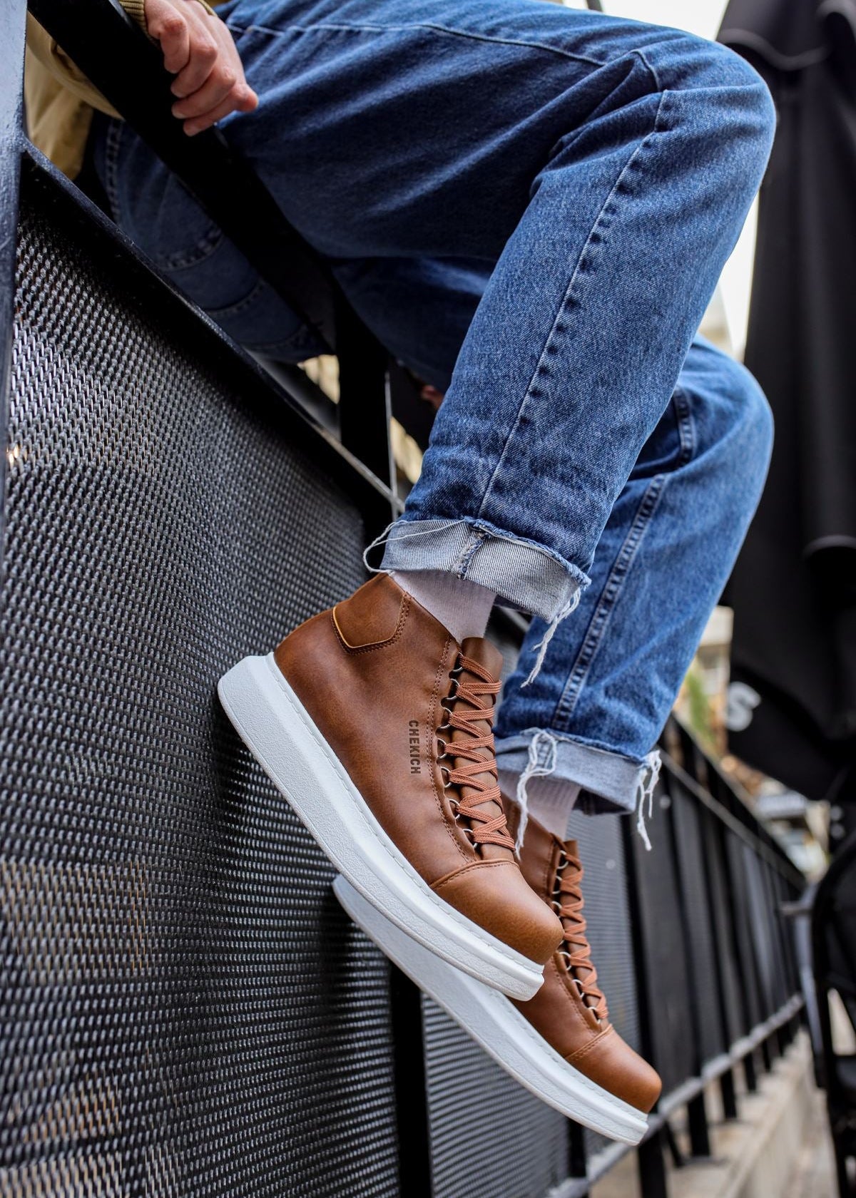 Brown leather sneakers with white soles worn by a person on a metal staircase.