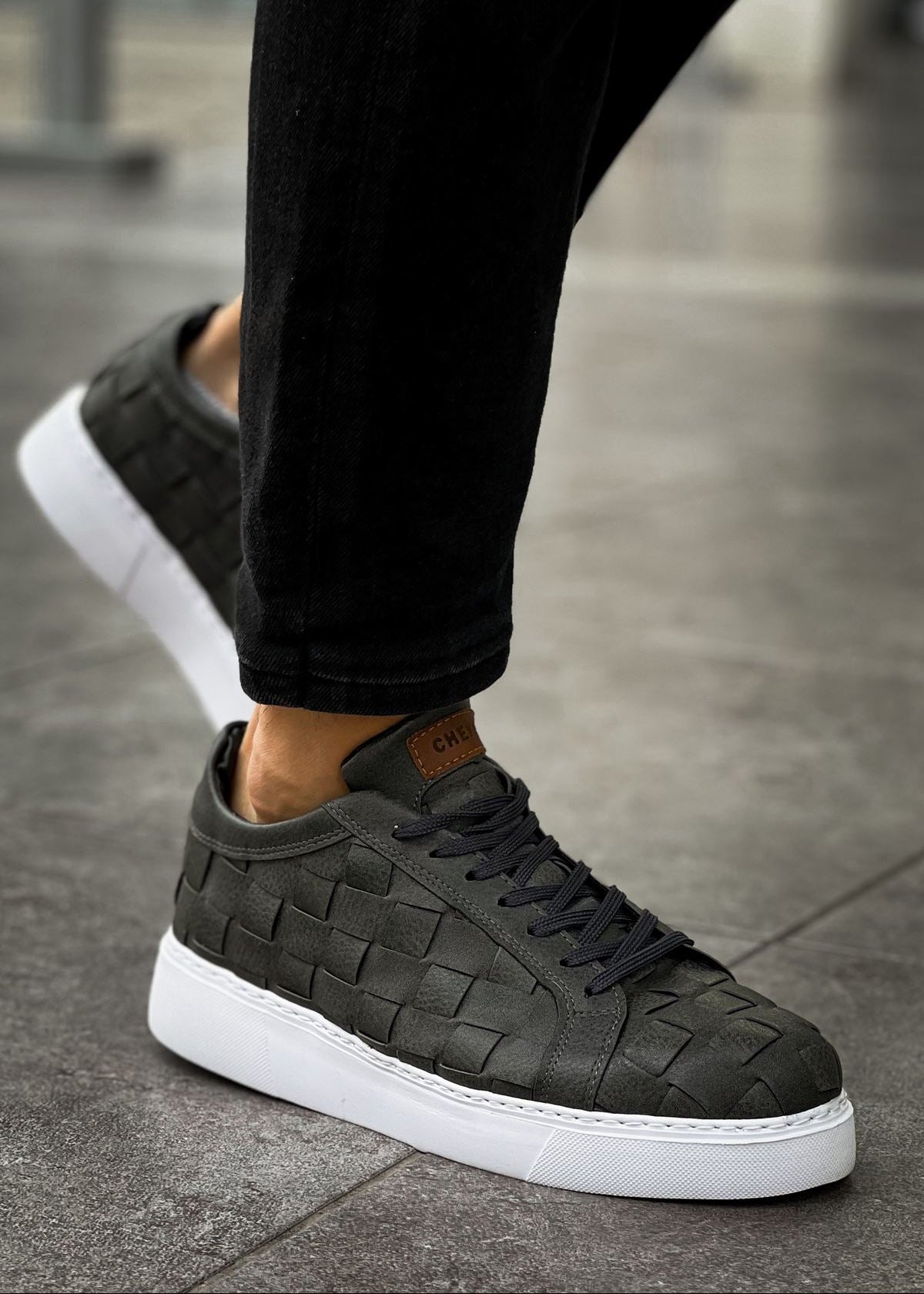 A pair of 'Zeus Grey Weave' sneakers with a grey vegan leather upper and a woven pattern, featuring a white sole and lace-up closure.