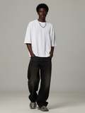 Person wearing a white oversized t-shirt and black pants on a plain background