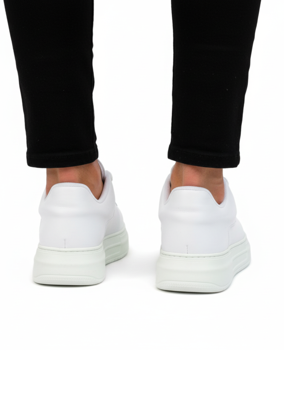 White sneakers worn with black pants on a white background