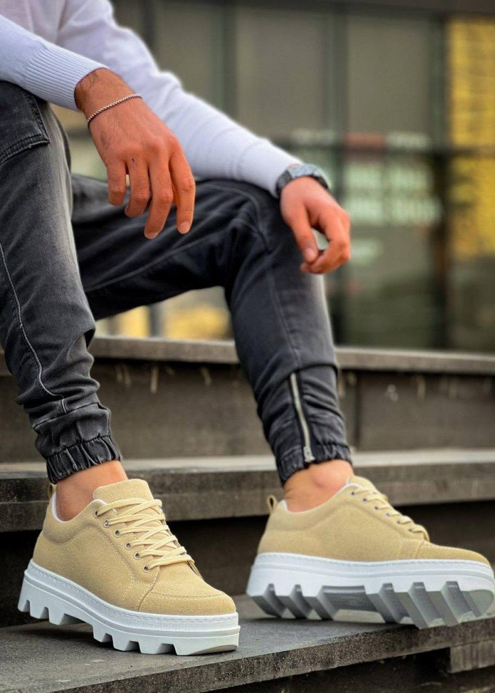 Beige sneakers with white soles worn by a person sitting on steps.