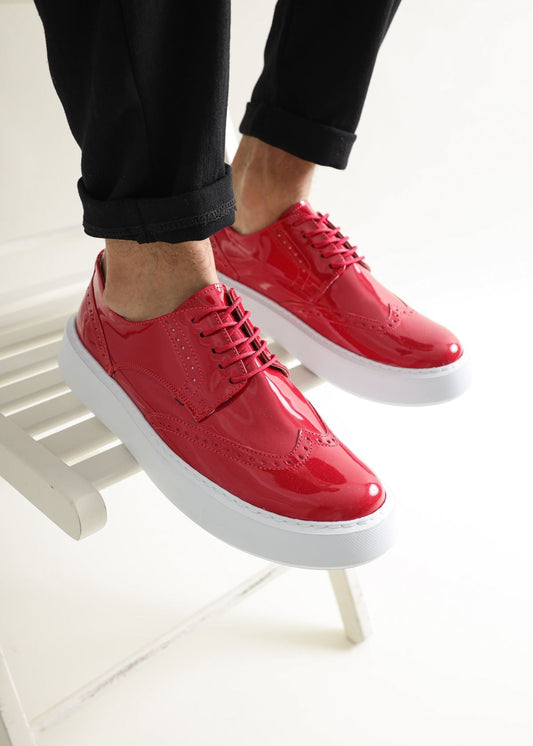 A pair of men's red patent leather dress shoes with white soles, worn by a model.