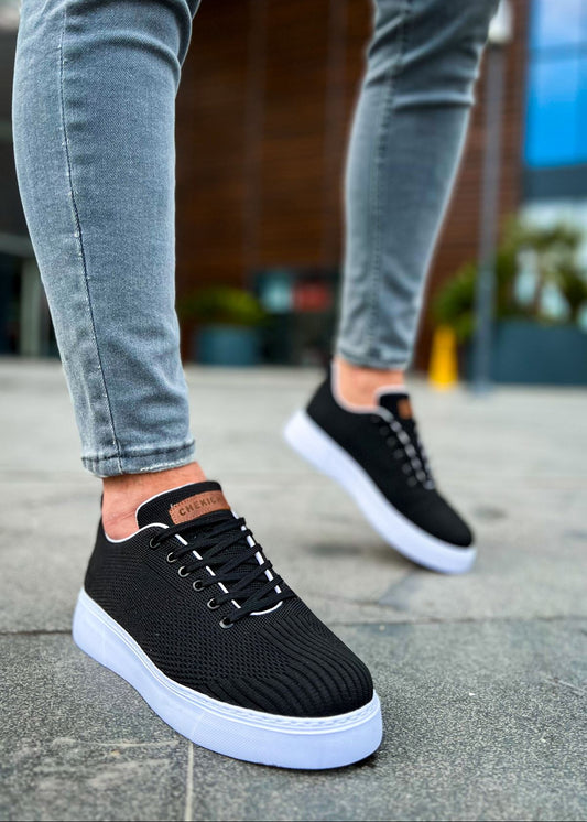 A pair of men's casual sneakers with black knitted upper and white soles, being worn by a person.