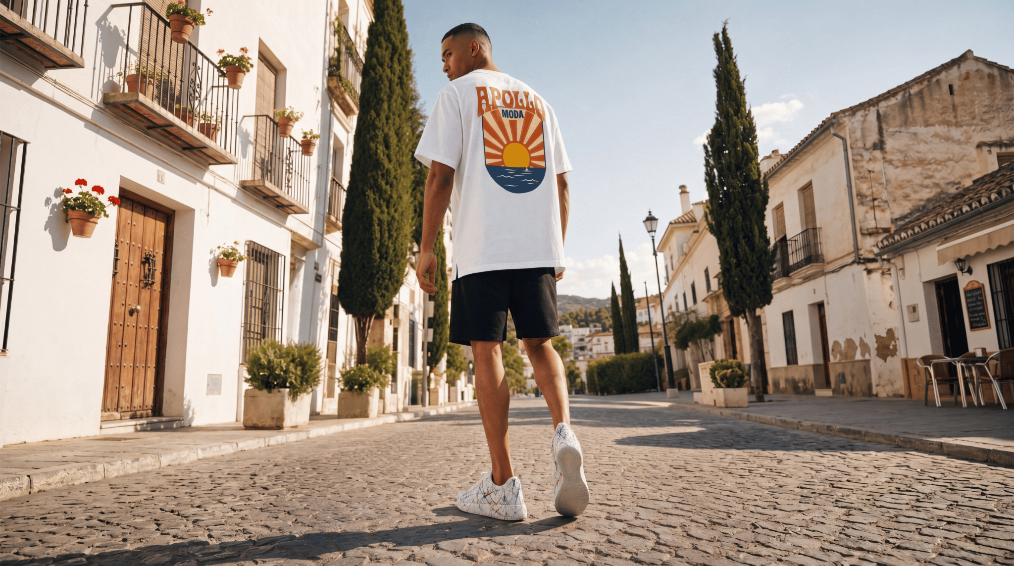Man walking on a cobbled street in a European town, wearing a white t-shirt with a colorful graphic design.