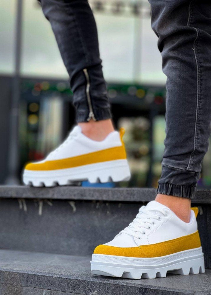 White sneakers with yellow accents worn by a person on steps.