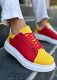 Red and yellow sneakers worn by a person sitting on a metal bench.