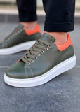 Green sneakers with orange accents worn by a person on a tiled floor.