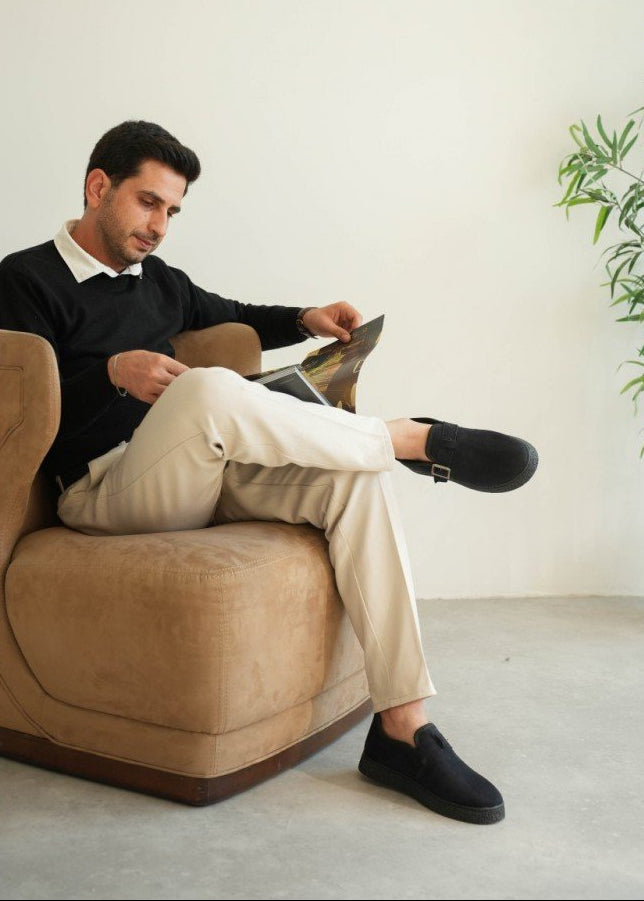 Man reading a magazine on a beige armchair in a minimalistic room.