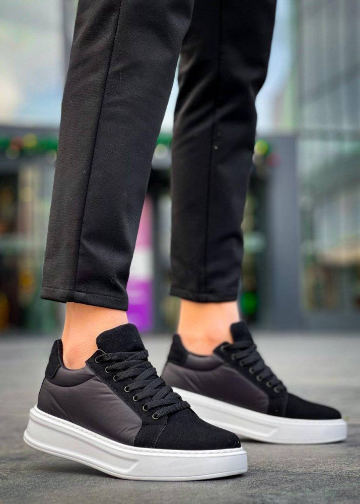 Black sneakers with white soles worn by a person on a blurred background
