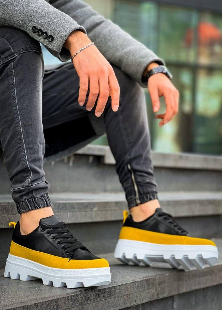 Black and yellow sneakers with white soles worn by a person sitting on steps.