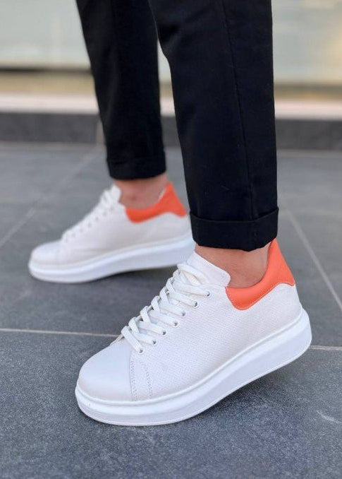 White sneakers with orange accents worn on a gray pavement.