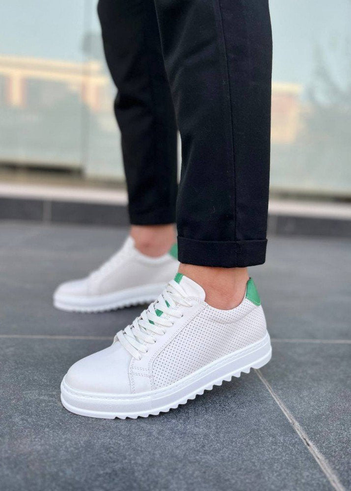 White sneakers with green accents worn on a gray pavement.