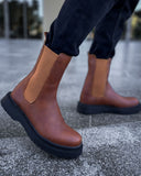 Brown leather boots with black soles worn by a person on a concrete surface.