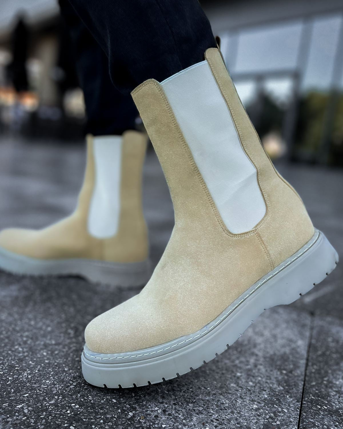 Lifestyle shot of Zenith Sand Chelsea Boots by Apollo Moda in beige suede with white elastic panels and gray soles worn outdoors.