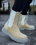 Lifestyle shot of Zenith Sand Chelsea Boots by Apollo Moda in beige suede with white elastic panels and gray soles worn outdoors.