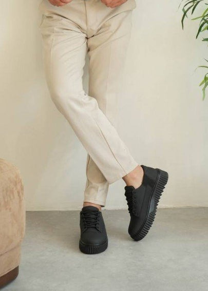 Person wearing black chunky sneakers with beige pants on a neutral background